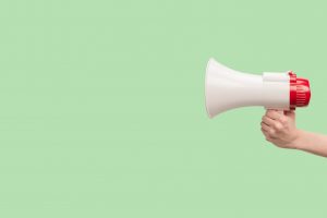Megaphone in woman hands on a green background.