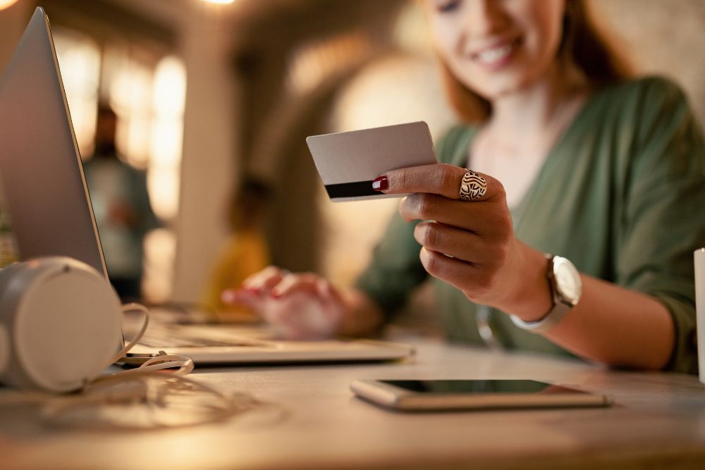 Fidelização no e-commerce Mulher sorridente segura um cartão de crédito enquanto digita em um notebook, representando a satisfação e confiança geradas pela fidelização no e-commerce