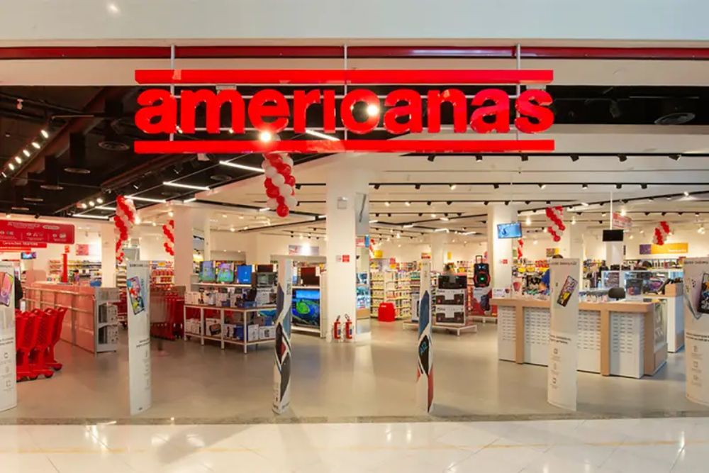 marketplace físico Fachada de uma unidade da Lojas Americanas, com letreiro vermelho característico sobre fundo branco, representando o varejo físico tradicional da marca que aposta no marketplace físico.