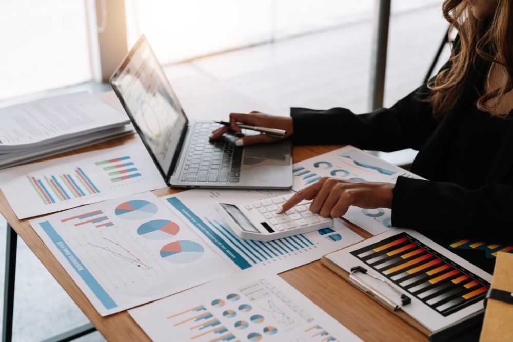 Relatórios GA4 Profissional de marketing em uma mesa de trabalho analisando gráficos e usando uma calculadora para extrair insights valiosos dos relatórios GA4 em seu notebook.