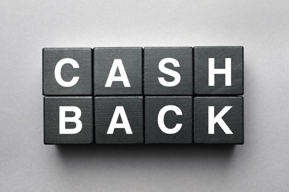 cashback Caixas de madeira pretas com a palavra "CASHBACK" escrita em branco, dispostas em duas linhas sobre um fundo cinza.
