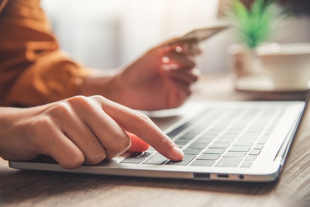 Checklist Black Friday Mãos de uma pessoa digitando em um laptop enquanto segura um cartão de crédito, simbolizando a etapa final de um Checklist Black Friday no checkout.