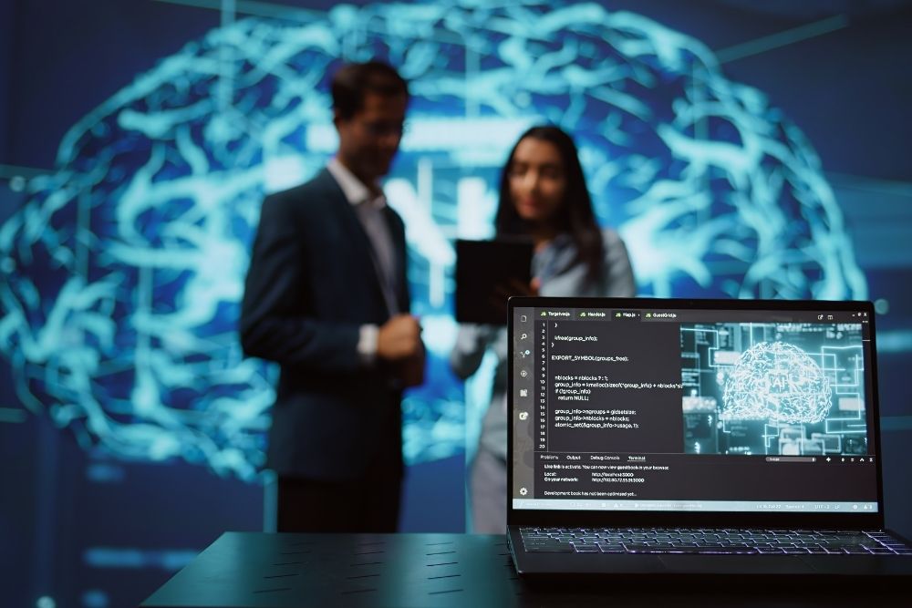 Tendências de IA Profissionais em ambiente tecnológico analisam tendências de IA, com um laptop exibindo código em primeiro plano e uma projeção de cérebro digital ao fundo.