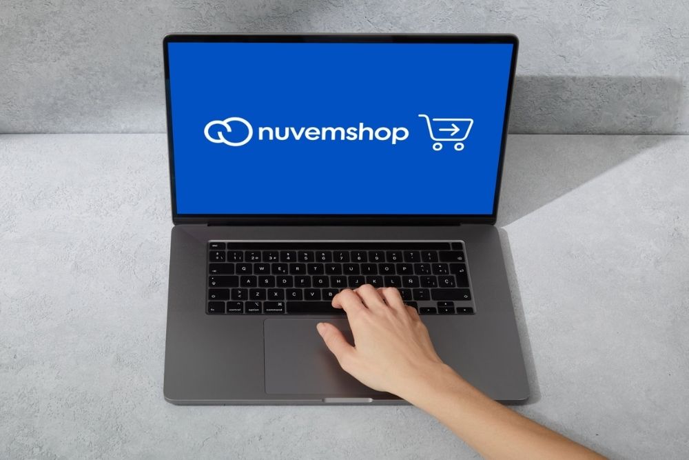 checkout acelerado Nuvemshop Pessoa operando um notebook com tela azul exibindo o logotipo da plataforma e um ícone de carrinho de compras, representando a gestão do checkout acelerado nuvemshop.