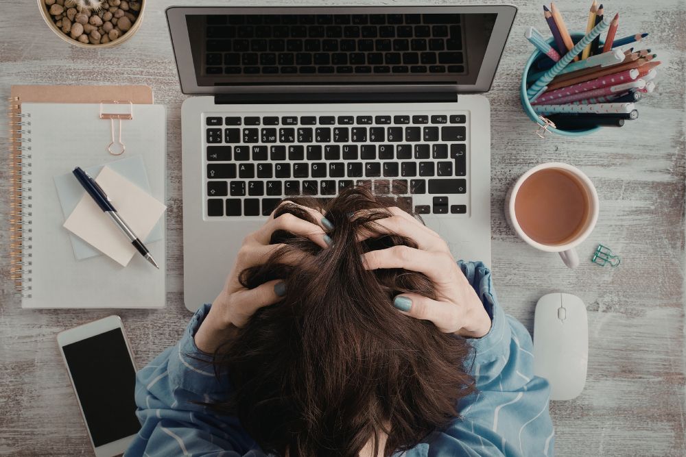 crescer sem eficiência Pessoa com a cabeça baixa sobre o teclado do notebook, representando o estresse de crescer sem eficiência no e-commerce
