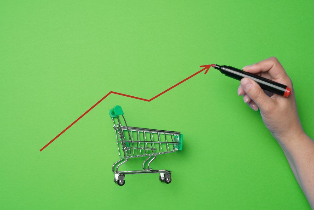 taxa de conversão Mão desenhando um gráfico vermelho de crescimento sobre um carrinho de compras em miniatura em um fundo verde, representando o aumento da taxa de conversão no e-commerce.