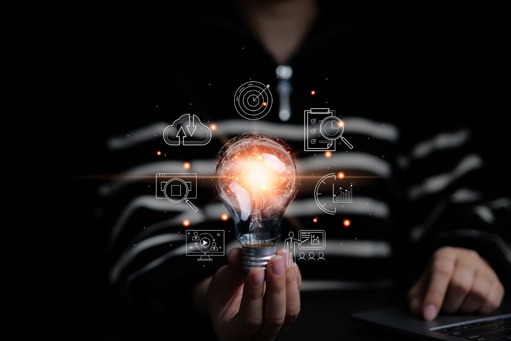 Mão segurando uma lâmpada iluminada cercada por ícones digitais de estratégia, análise de dados e tecnologia, representando a inteligência e a visão integrada do modelo CS Flex.